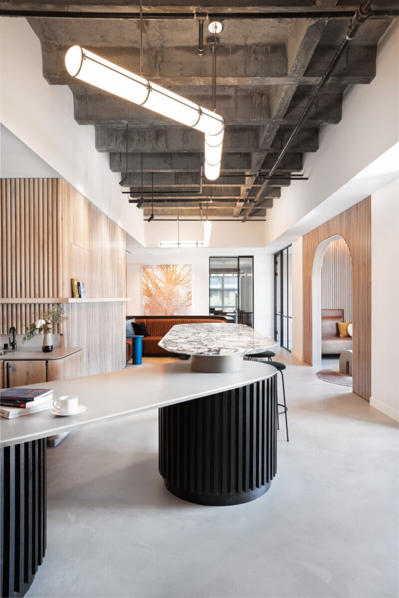 Custom reception area with fluted woodwork and marble countertops below designer lighting in a modern office space in San Francisco.