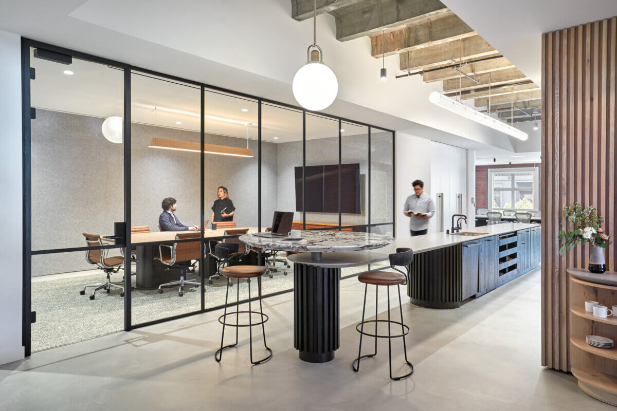 A sleek, modern kitchen area and extra long island provide a gathering space in a modern office.