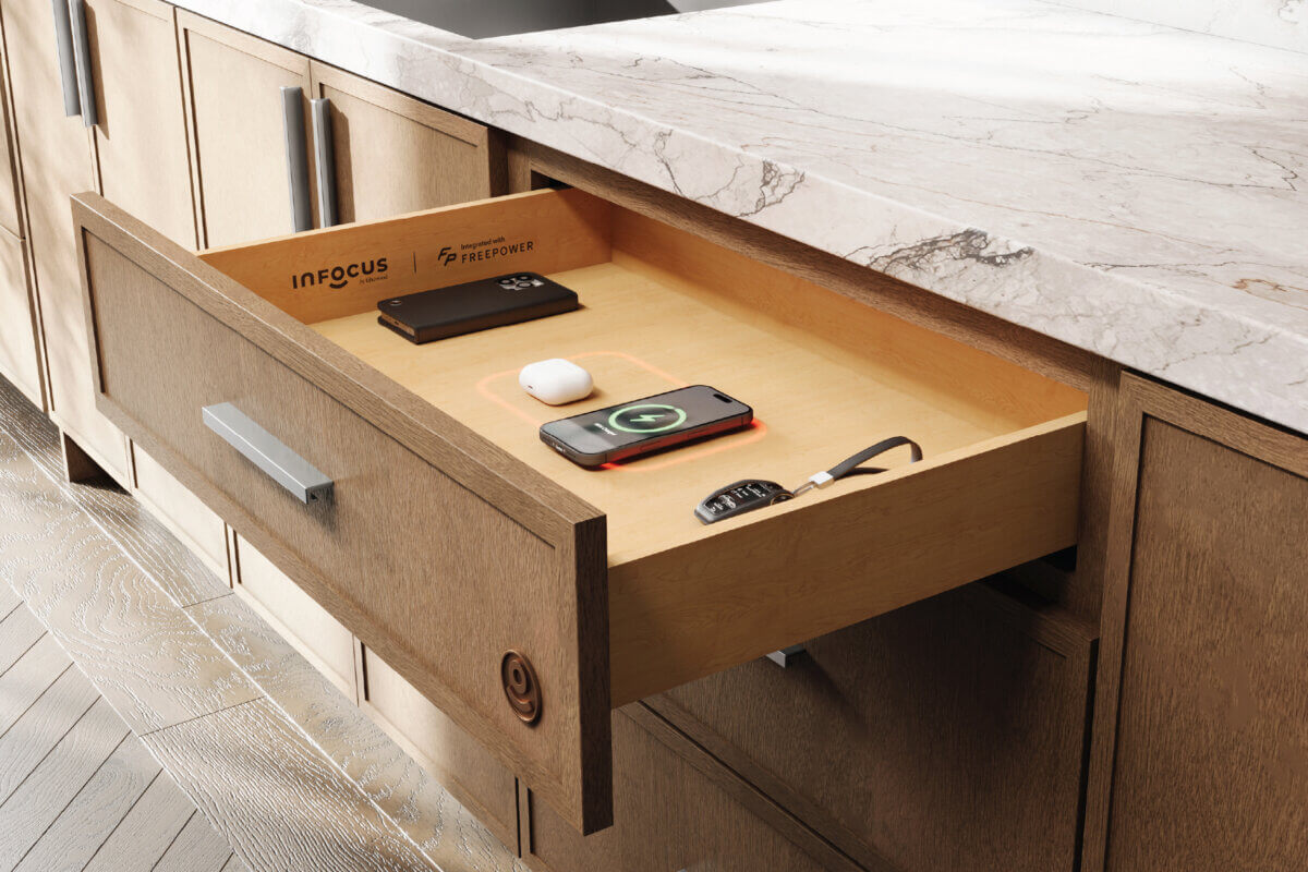 Pictured: the InFocus Drawer, powered by FreePower, integrated into a Fabuwood kitchen with a Desert Oak island. The phone charges out of sight while the countertop stays clear, warm, and uninterrupted.