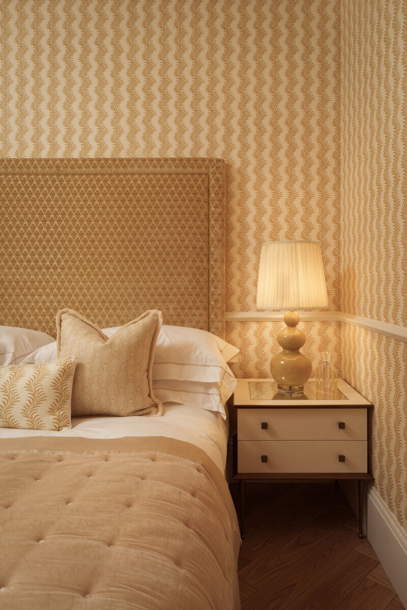 A bedroom designed by Mark Howorth: warm yellows and beiges on the wall, bed cover, and side table.