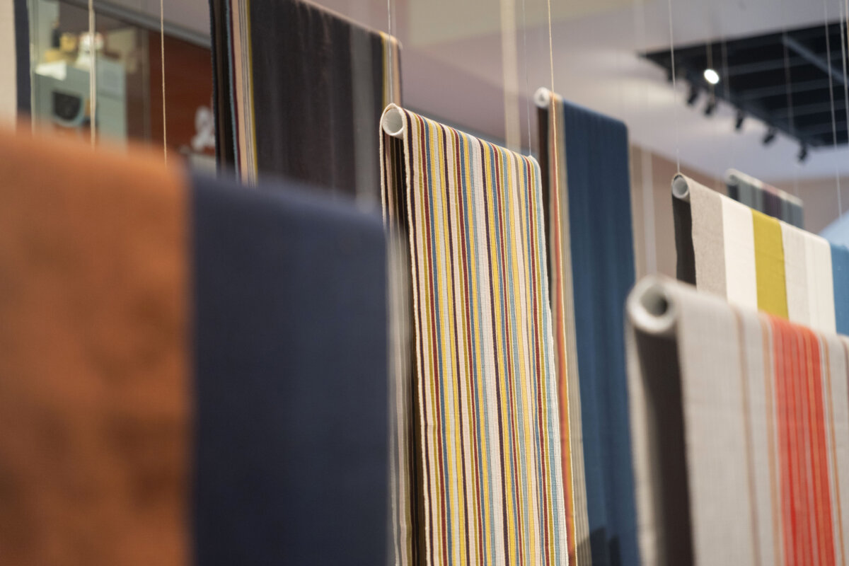 A display of hanging textile samples in a range of colors and patterns, including navy, rust, mustard, cream, and multicolored stripes, showcasing fabric textures and finishes.